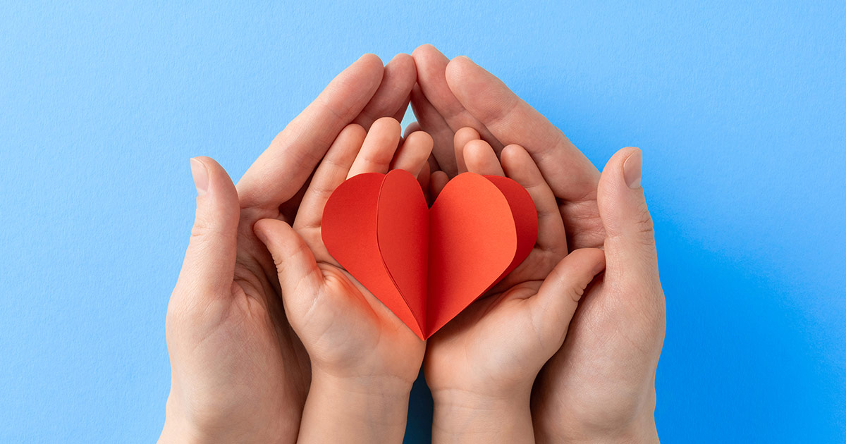 Multiple hands gently surround a red paper heart against a soft blue background. The image symbolises compassion, support, inclusion and the positive impact of community services, reflecting careers focused on helping individuals and strengthening communities.